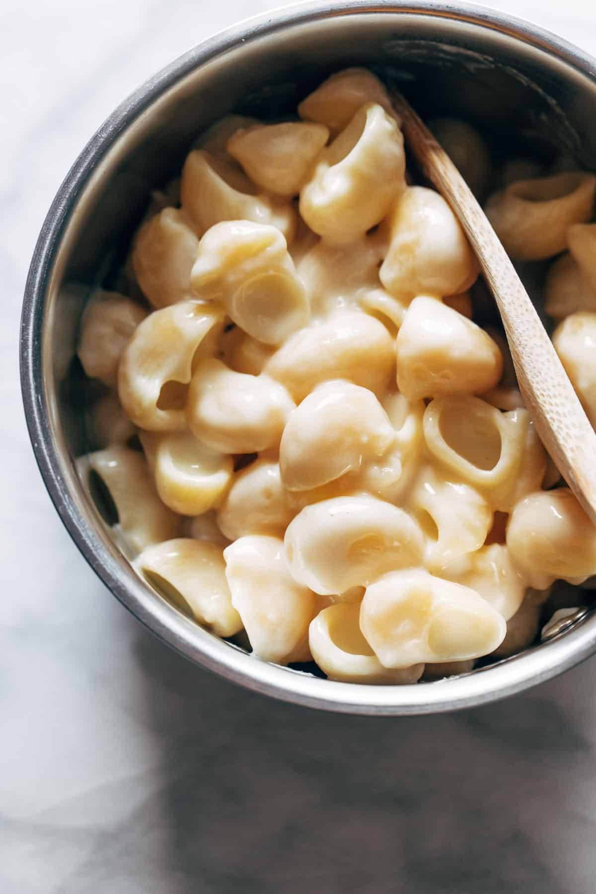 A bowl of shell pasta with wooden spoon.